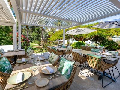 Outdoor restaurant area with set tables and plants under a pergola.