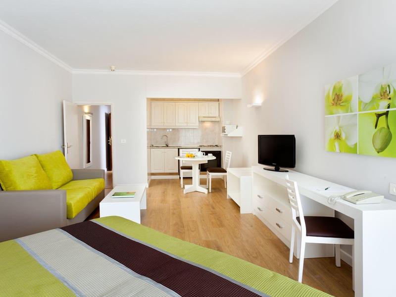 Modern hotel room with bed, desk, and seating area in bright colors.