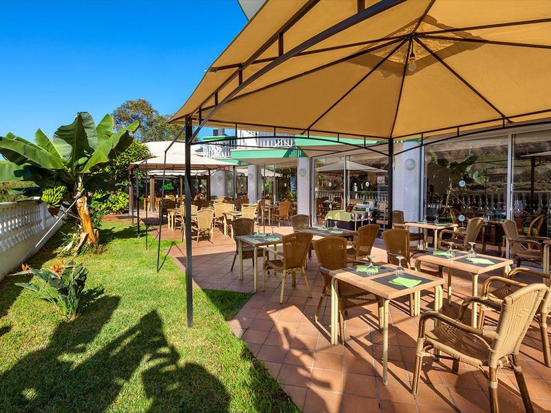 Sunny outdoor restaurant terrace with tables, chairs, and large umbrellas.