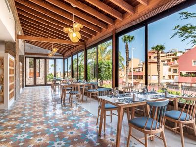 Salle à manger lumineuse avec tables et chaises en bois, grandes fenêtres et sol carrelé décoratif