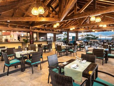 Espace extérieur moderne d'hôtel avec tables dressées et vue sur la mer au coucher du soleil.