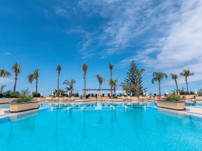 Grande piscine extérieure avec parasols et palmiers sous un ciel bleu dans une station balnéaire.