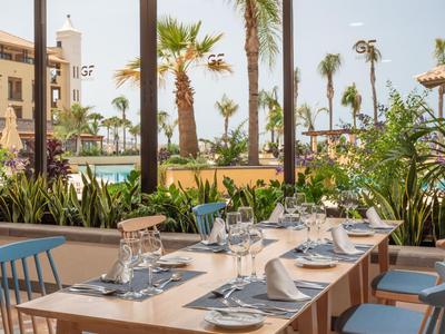 Espace repas avec tables dressées et vue sur des palmiers et la mer en arrière-plan.