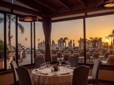 Un restaurant élégant avec vue sur une terrasse et le coucher de soleil au bord de la mer.