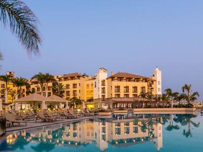 Hotel di lusso con grande piscina e palme al tramonto.