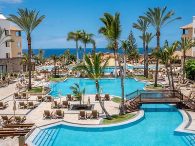 Grand piscine d'hôtel avec des palmiers et vue sur la mer sous un ciel bleu clair.