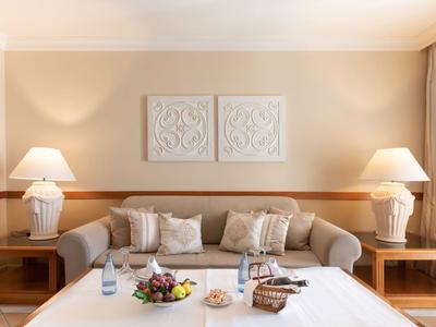 Salon confortable avec canapé beige, deux lampes et une table dressée avec fruits et snacks.