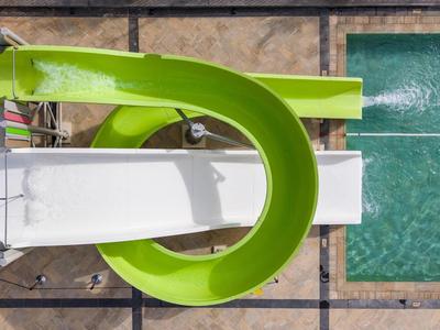 Toboggan aquatique vert menant à une piscine rectangulaire entourée de dalles en pierre.
