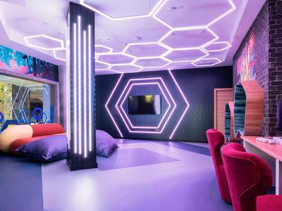 Chambre moderne avec murs éclairés au néon, lit, bureau et chaises rouges.