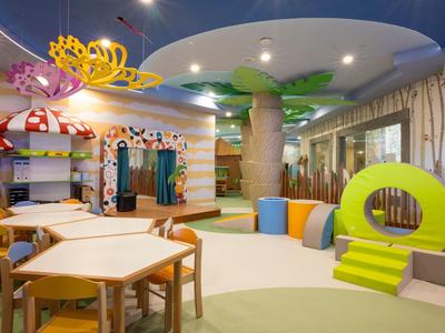 Espace de jeu pour enfants coloré avec tables, chaises et décorations imaginatives dans un hôtel.