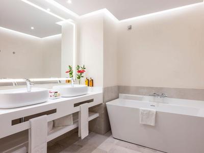Salle de bain d'hôtel moderne avec baignoire, lavabo et arrangement floral sur le comptoir.