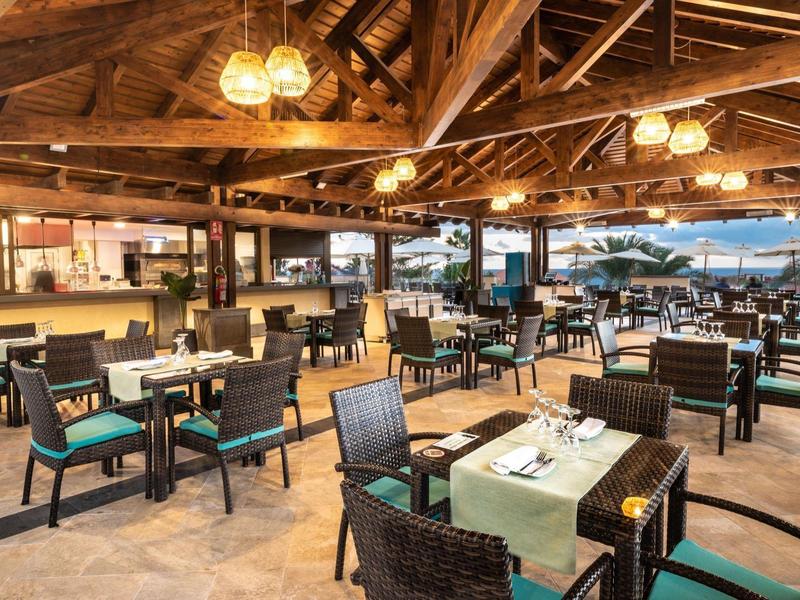 Espace extérieur moderne d'hôtel avec tables dressées et vue sur la mer au coucher du soleil.