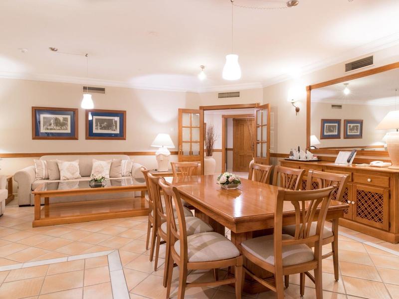 Salle à manger lumineuse avec table et chaises en bois, canapé et grands miroirs aux murs.