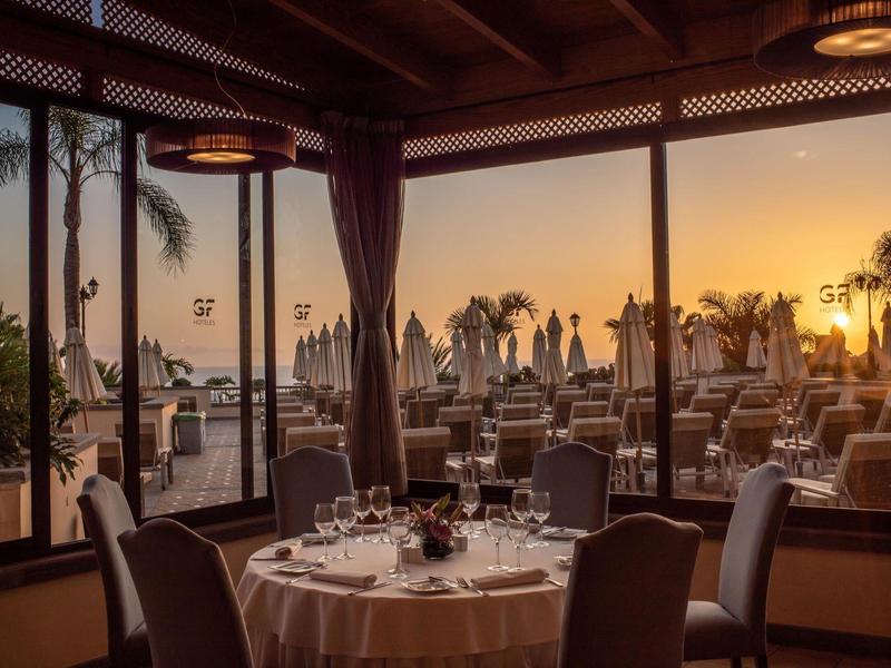 Un restaurant élégant avec vue sur une terrasse et le coucher de soleil au bord de la mer.