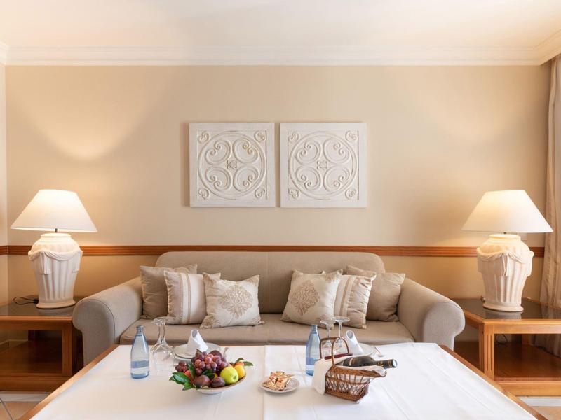 Salon confortable avec canapé beige, deux lampes et une table dressée avec fruits et snacks.