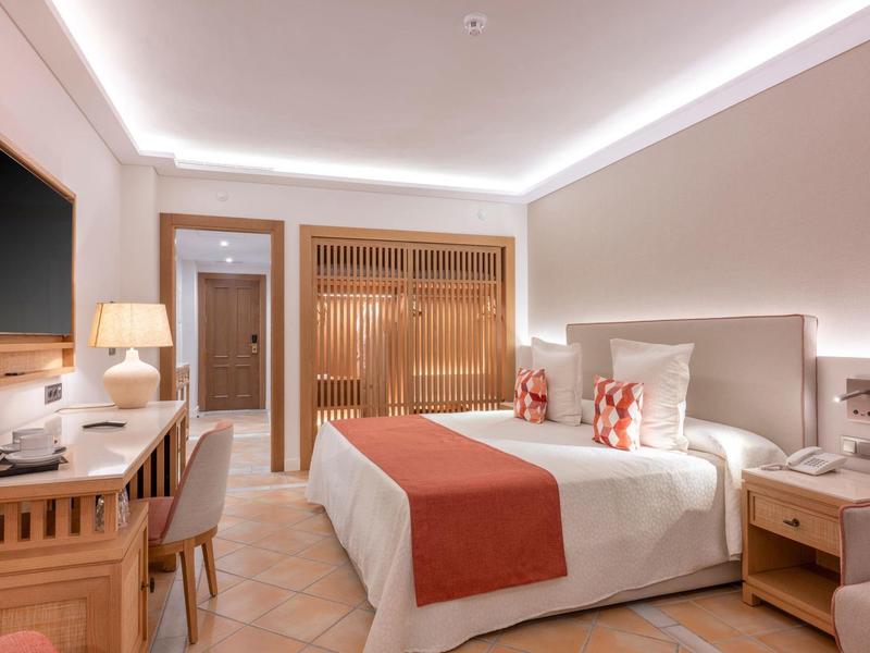 Chambre d'hôtel lumineuse avec lit double, mobilier en bois et éclairage d'accent au plafond.