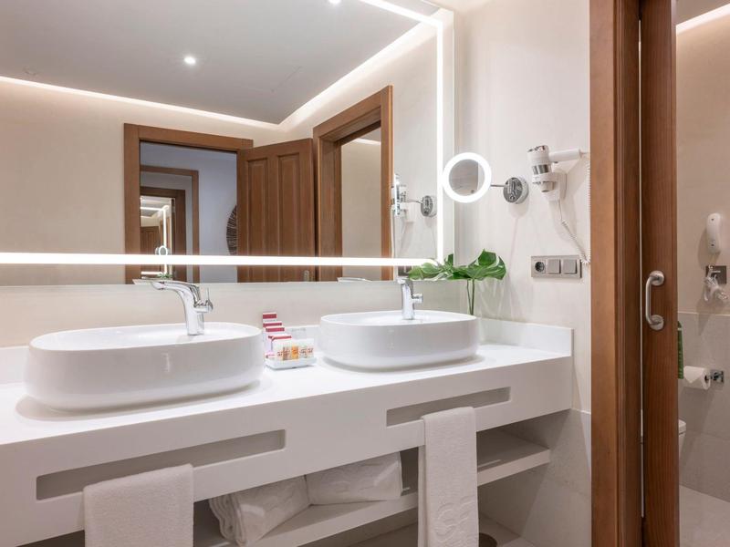 Salle de bain moderne avec doubles vasques, miroir éclairé et tons blancs.