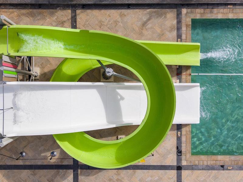 Toboggan aquatique vert menant à une piscine rectangulaire entourée de dalles en pierre.