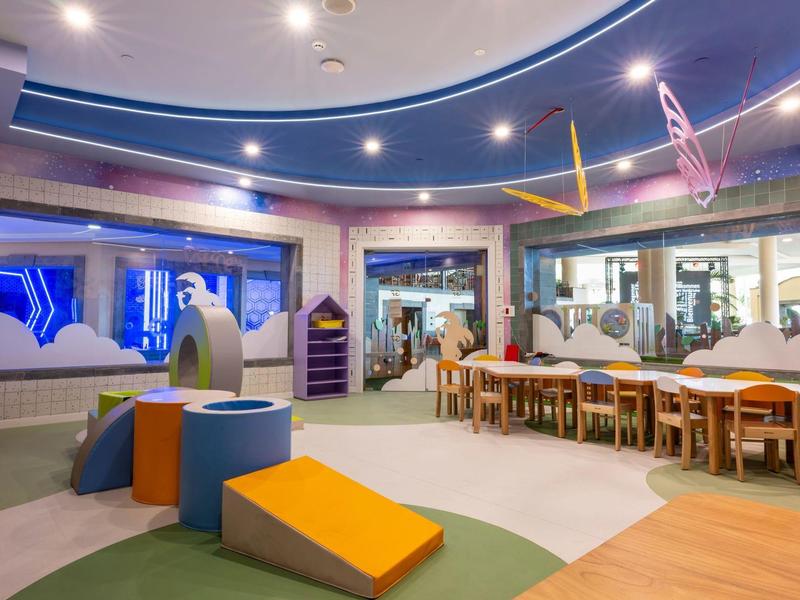 Espace de jeux pour enfants moderne et colorée dans un hôtel avec tables et mobilier de jeu.