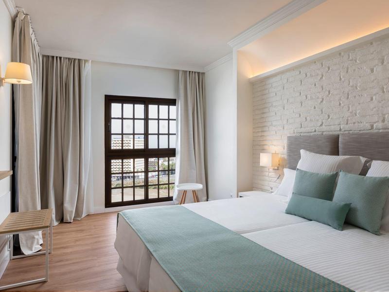 Modernes Schlafzimmer mit großem Bett, weißen Wänden, Holzfußboden und Fenster mit Vorhängen.