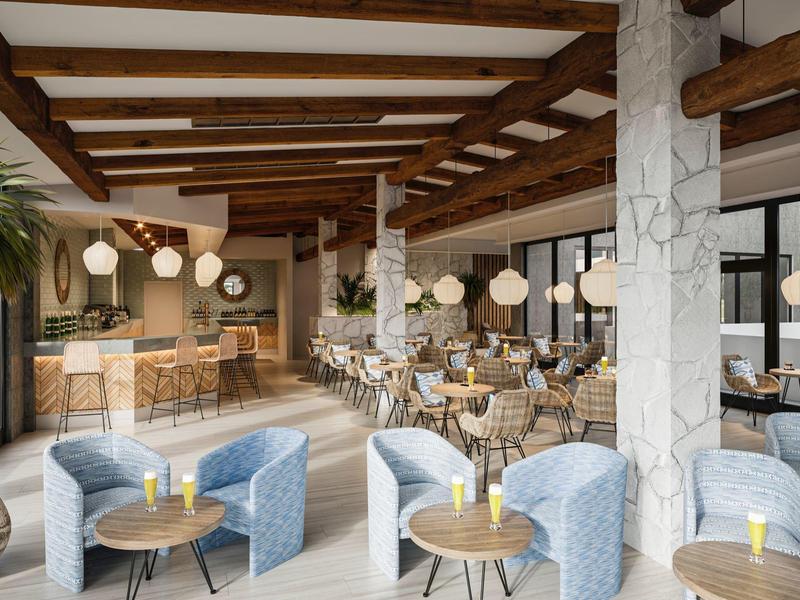 Moderner Cafébereich mit blauen Sesseln, Holzdeckenbalken und rundem Mobiliar in warmen Tönen.