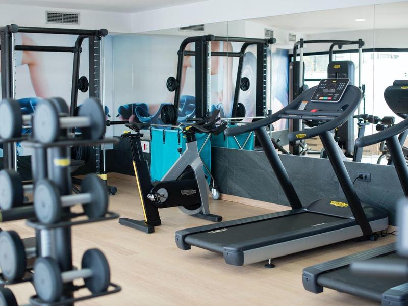 Modern gym with treadmills, exercise bikes and free weights near large windows.