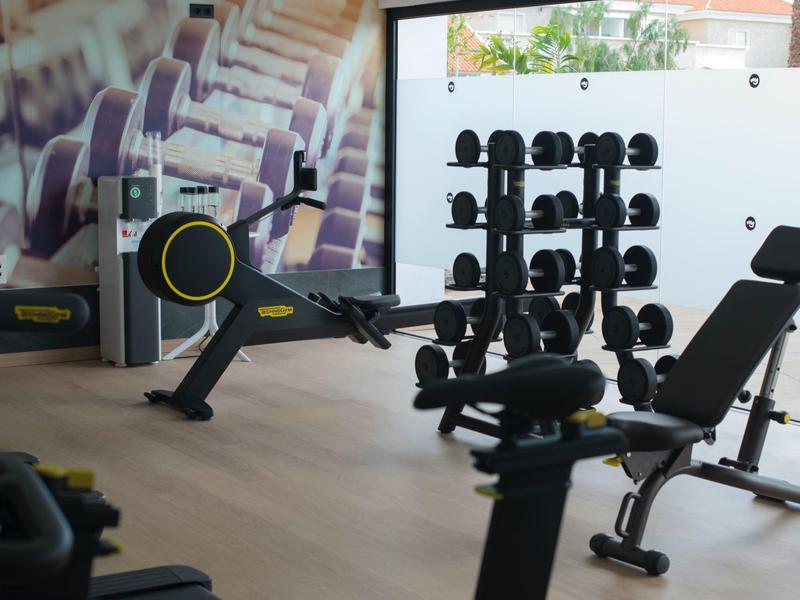 Modern gym with free weights, benches, and cardio equipment near a large window.