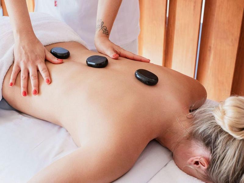 Person receiving hot stone massage with black stones placed on back, lying face down on white towel.
