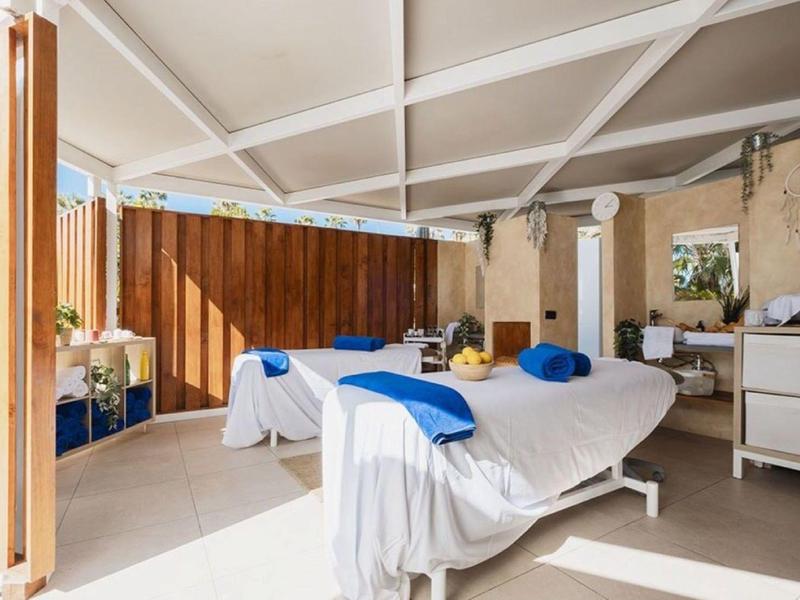 Bright massage room with two tables, blue towels, and natural light from wooden panels.