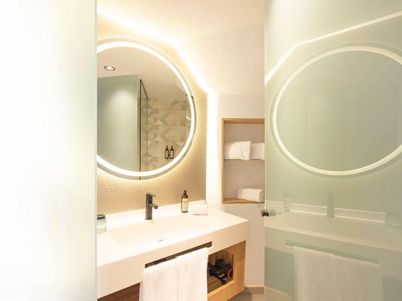 Modern bathroom with illuminated round mirror, white countertop, and neatly folded towels.