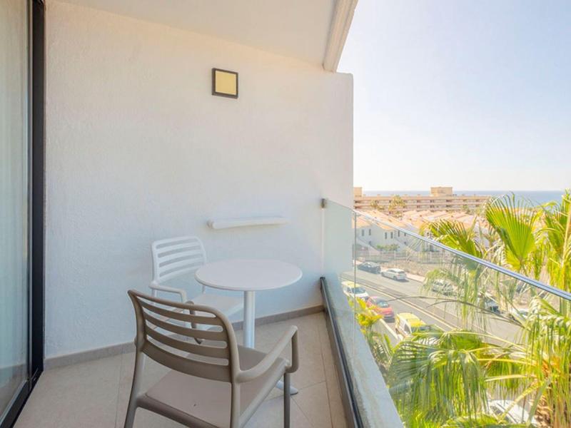 Small balcony with two chairs and table overlooking a sunny coastal area.