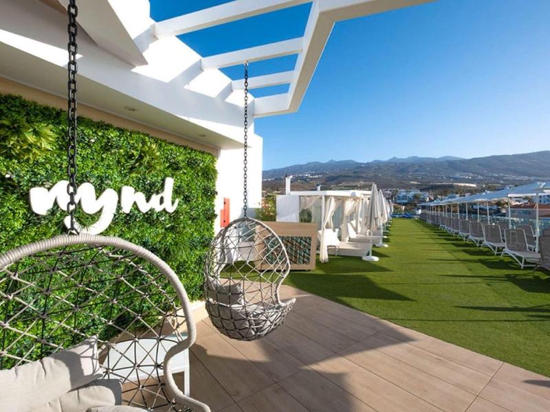 Roof terrace with hanging chairs, artificial grass, and a sea view under clear skies.