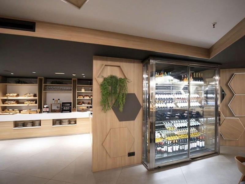 Modern hotel bar area with well-lit shelves and refrigerated display filled with wine bottles.