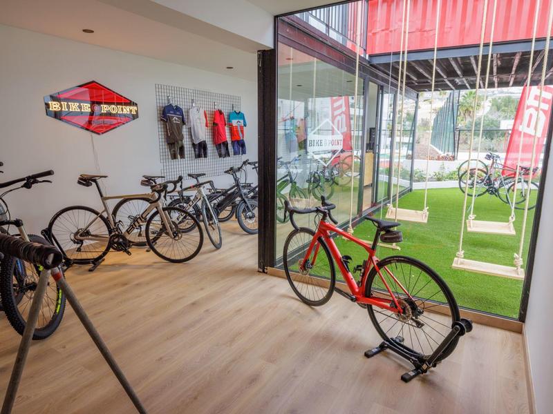 Bike rental area with several bicycles inside a glass-walled room, green space outside.
