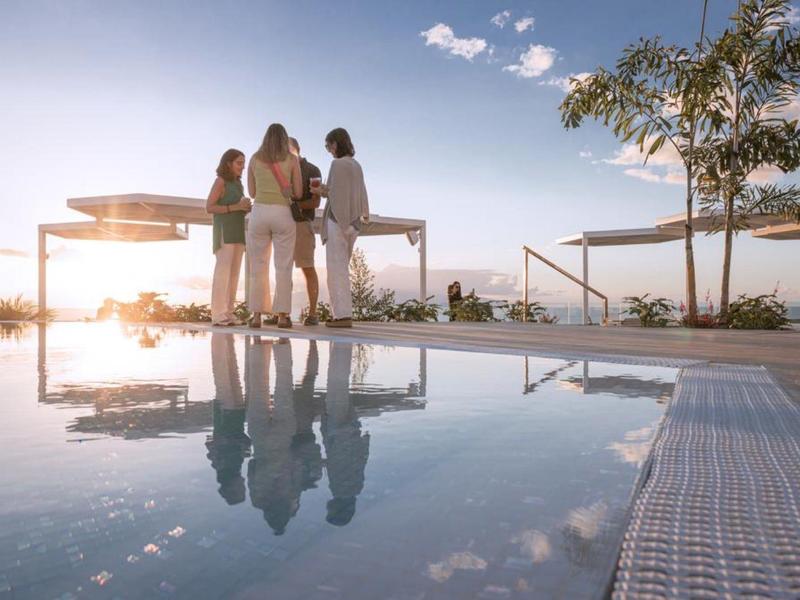 Four people standing near a pool at sunset with clear sky and modern structures.