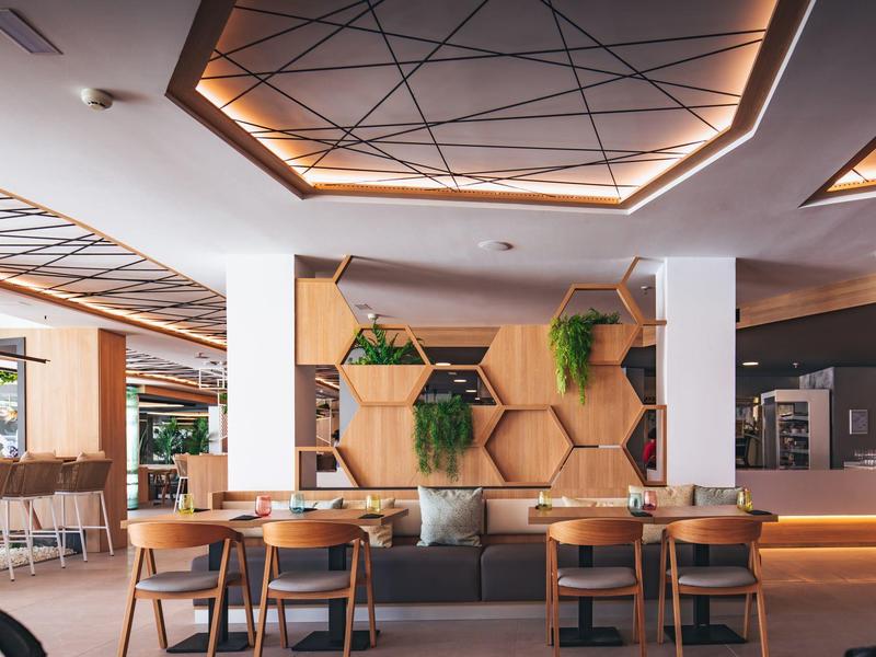 Modern hotel lobby with wooden decor, hanging plants, and seating area with chairs and couches.