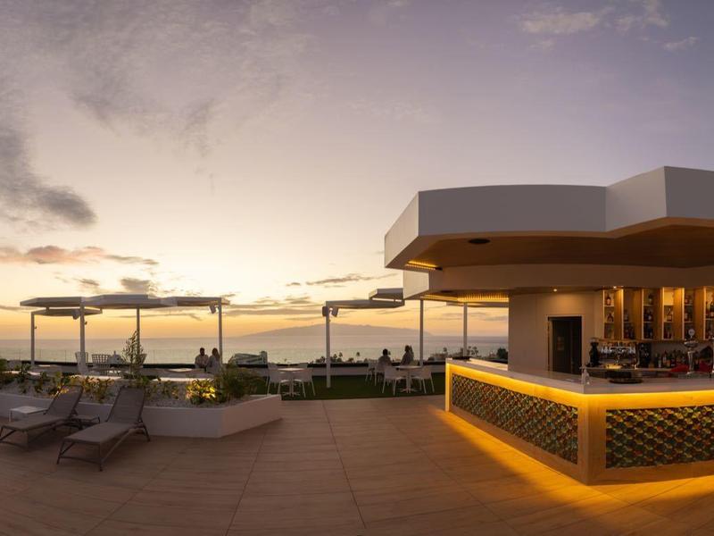Sunset view of a beachside hotel bar with loungers and palm trees along the shore.