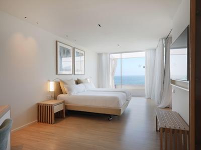 Helles Schlafzimmer mit Doppelbett, Holzboden, großen Fenstern und Meerblick.