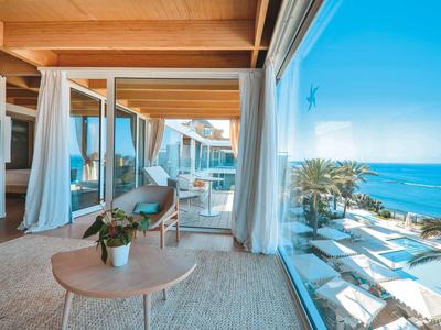 Modernes Zimmer mit Holzbalken, großen Fenstern und Meerblick, heller Möbel und weißen Vorhängen.