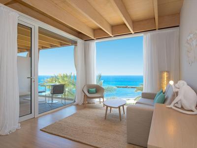 Helles Wohnzimmer mit Holzdecke, großem Fenster, Blick aufs Meer, bequemer Couch und modernem Ambiente.