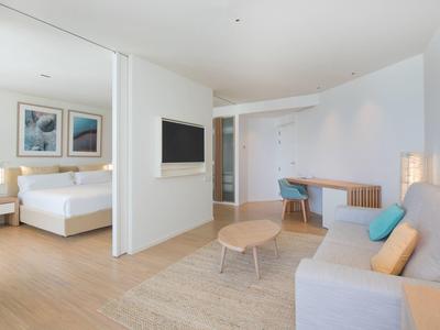 Helles, modernes Hotelzimmer mit Doppelbett, Sofa, Schreibtisch und Holzfußboden.
