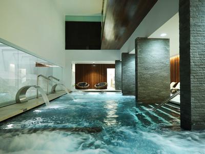 Modernes Hallenbad mit klarem Wasser, grauen Steinwänden und indirekter Beleuchtung.