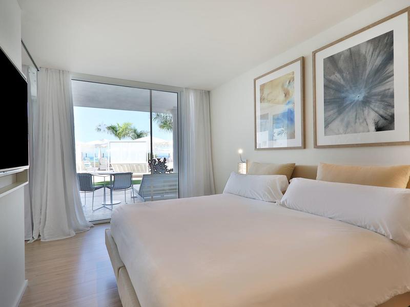 Helles Schlafzimmer mit großem Bett, zwei Bildern an der Wand und Balkon mit Außenmöbeln.