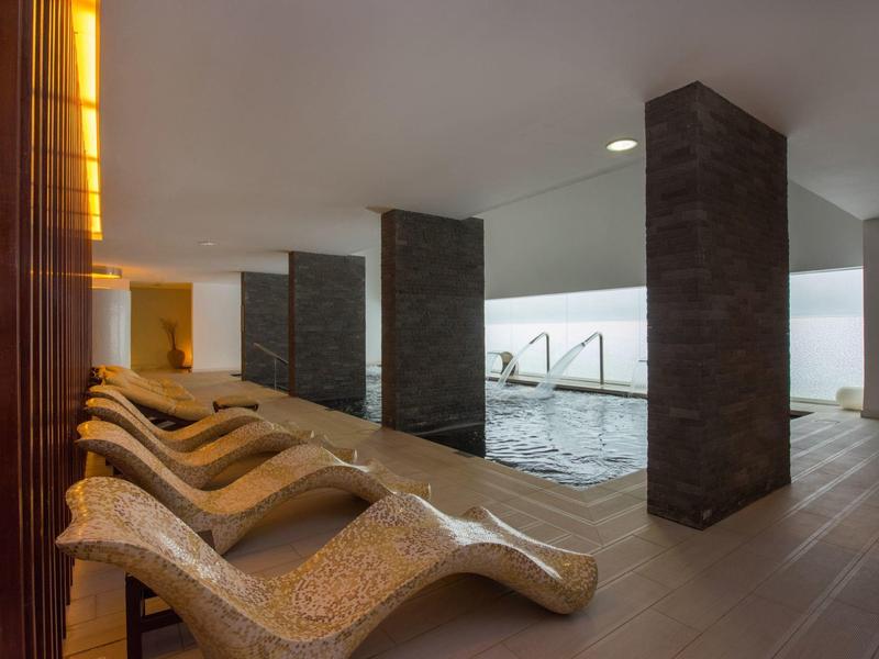 Innenraum eines Wellnessbereichs mit Liegen und Schwimmbecken, moderne helle Gestaltung.