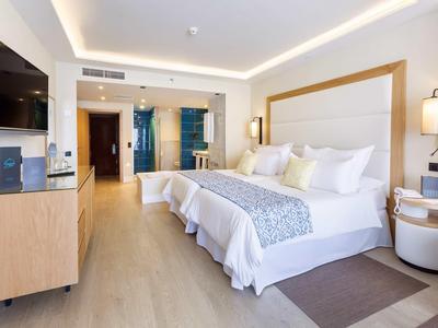 Camera d'hotel ben illuminata con due letti, TV, scrivania e bagno moderno.