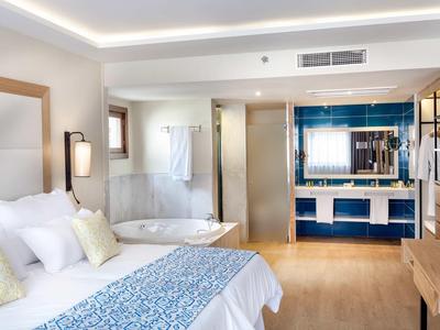 Camera d'hotel luminosa con letto grande, vasca da bagno e zona lavabo moderna con piastrelle blu.