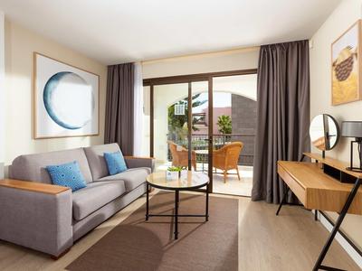 Soggiorno luminoso con divano grigio, tavolino e accesso a terrazza con mobili da giardino.