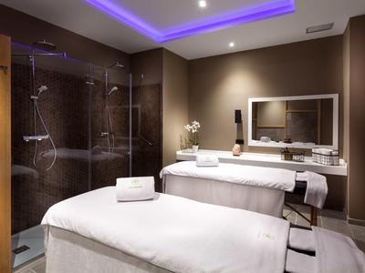 Camera spa moderna con due lettini, illuminazione soffusa e doccia in vetro.