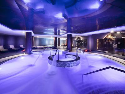 Area spa moderna con idromassaggio illuminato e zone relax in un'atmosfera scura.