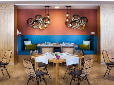 Ristorante moderno con sedie colorate e tavoli rotondi davanti a una parete blu-arancione.